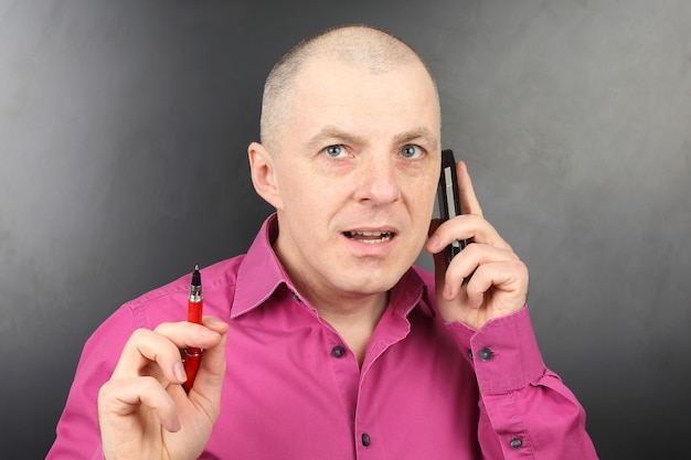 Zakenman in een roze shirt met een pen in de hand praten over een mobiele telefoon