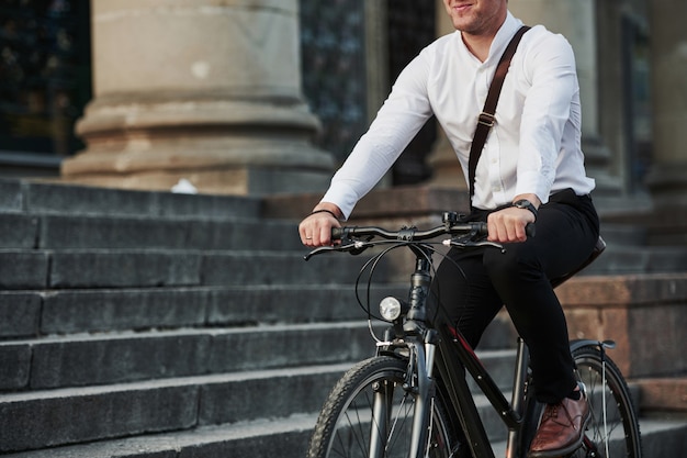 Zakenman in formele kleding met zwarte fiets is in de stad.