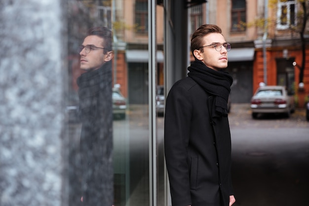 Zakenman in glazen en warme kleren in de buurt van het gebouw