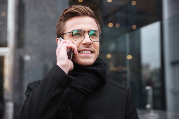 Zakenman in glazen met telefoon in de buurt van het kantoor.