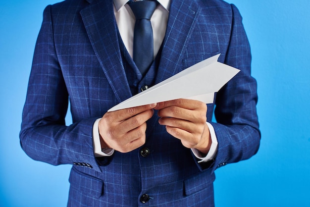 Zakenman in pak houdt papieren vliegtuigje in de hand op blauwe studio achtergrond. Ontwikkelingsconcept voor kleine bedrijven, projectlancering, teamtraining, start-ups, wereldwijde strategie, geen hoofdfoto