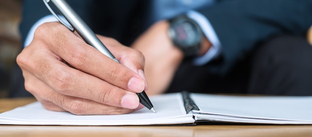 Zakenman in pak schrijven iets op notebook in kantoor of café, hand van man met pen met handtekening op papieren rapport. bedrijfsconcepten