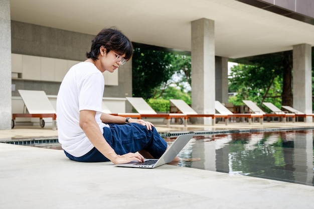 Zakenman in vrijetijdskleding met laptop aan het werk in de buurt van zwembad op vakantie Zakelijk werken op afstand
