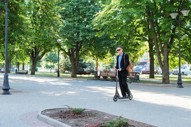 Zakenman in zonnebril met een tas rijdt door de straat op een scooter