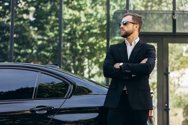 Zakenman in zwart pak bij zijn auto in de buurt van het kantoorcentrum.