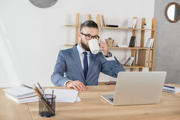 Zakenman koffie drinken tijdens het werken op de werkplek met laptop op kantoor