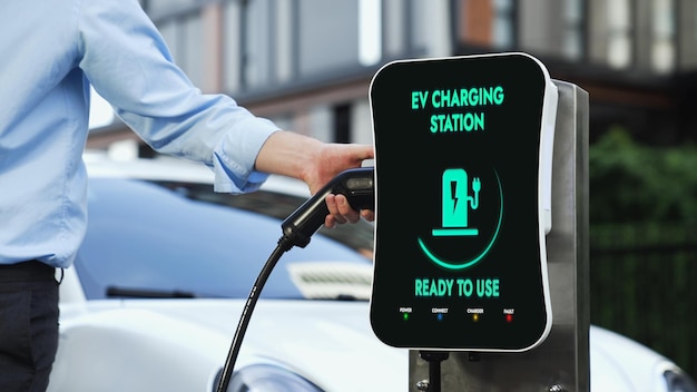 Zakenman laadt zijn elektrische auto op vanaf het laadstation in het stadscentrum of op een openbare parkeerplaats Eco-vriendelijke oplaadbare auto met behulp van alternatieve schone energie in de levensstijl van de stad