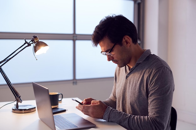 Zakenman laat aan het werk op laptop aan bureau met behulp van mobiele telefoon