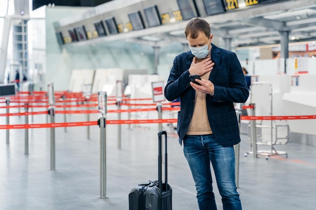 Zakenman loopt in luchthaventerminal heeft problemen met ademhalingscontroles e-mailbox op smartphone staat in de buurt van bagage draagt medisch wegwerpmasker als preventie van coronavirusuitbraak gezondheidsbewustzijn