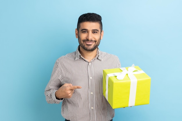 Zakenman met baard staande met gele geschenkdoos wijzende vinger kijkend naar camera