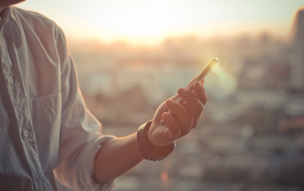 zakenman met behulp van een slimme telefoon handen zonsondergang hemel op wazig stedelijke stad als achtergrond