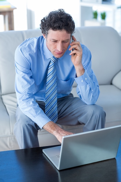 Zakenman met behulp van laptop en mobiele telefoon op de bank