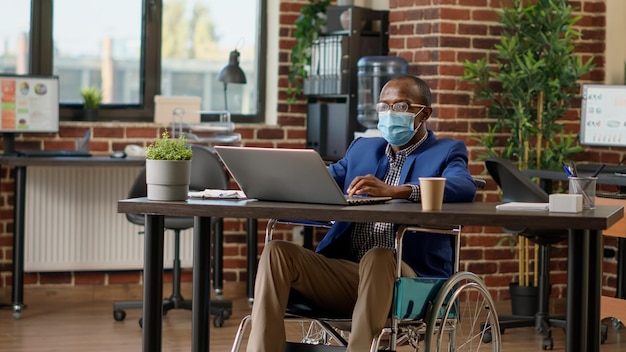 Zakenman met chronische handicap die opstartstrategie plant tijdens covid 19 pandemie. Werken in een gehandicaptenvriendelijk kantoor, lijdend aan lichamelijke beperkingen zittend in een rolstoel.