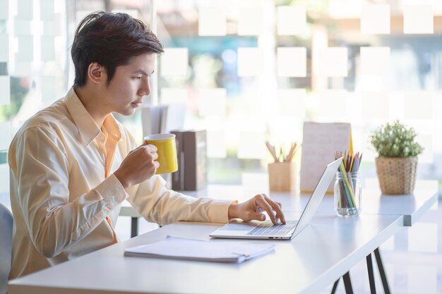 Zakenman met een koffiekop terwijl hij een laptop gebruikt op kantoor