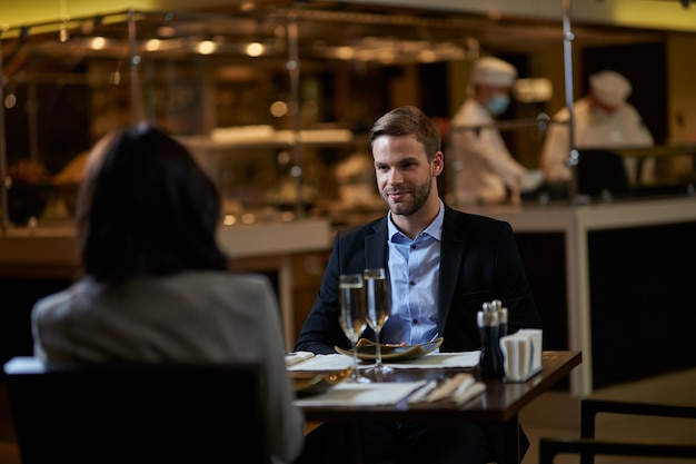 Zakenman met een officiële lunch met zijn vrouwelijke partner in restaurant met een paar volle wijnglazen ertussen