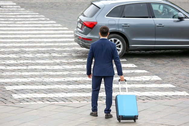 Zakenman met een reiskoffer loopt op een kruising van een stadsstraat