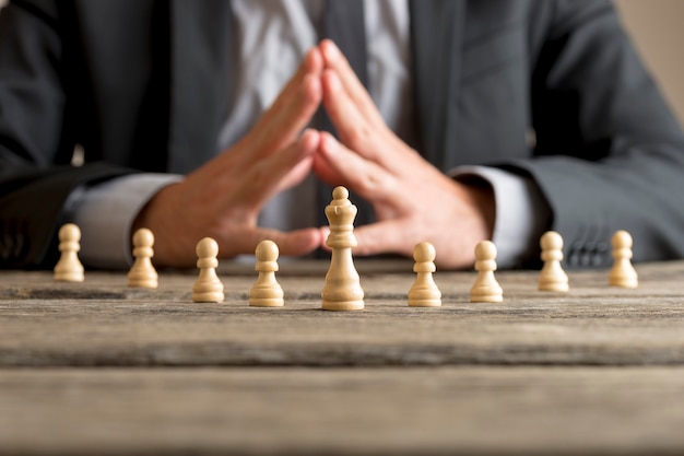 Foto zakenman met gevouwen handen planning strategie met schaken cijfers koningin en pionnen op een oude houten tafel.