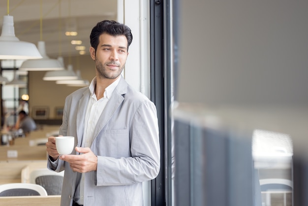 zakenman met kopje koffie kijkt uit raam op kantoor