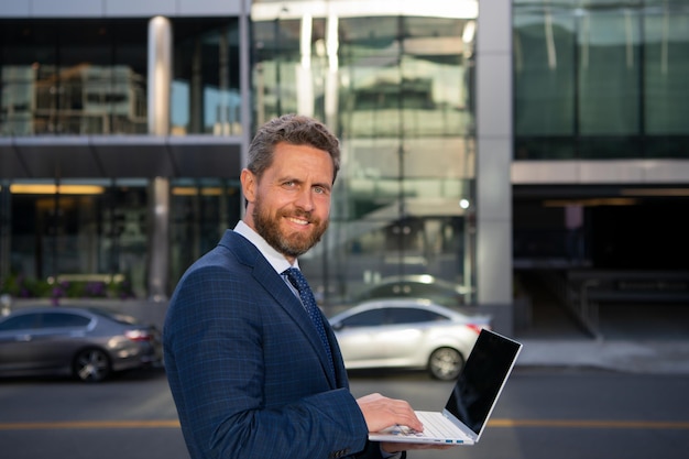 Zakenman met laptop op straat in de buurt van kantoorgebouw