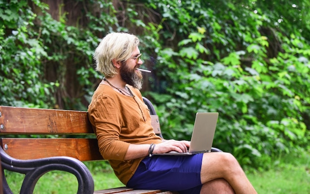 Zakenman met laptop zittend op een bankje in het park Knappe man aan het werk op laptop zakenman aan het werk buitenshuis met computer start videoconferentie communicatie via video-oproep Naar kennis