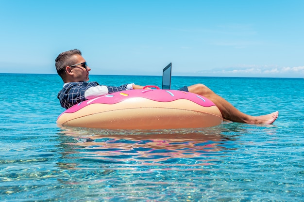 Zakenman met laptopcomputer op een opblaasbare donut in de zee