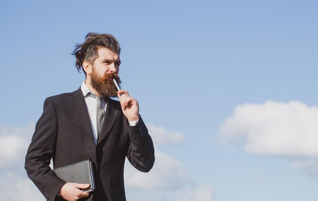 Zakenman met lucht Zakenman denkt aan iets met potlood Zakelijke dromen Doordachte jonge man in overhemd en stropdas met notitieblok en pen