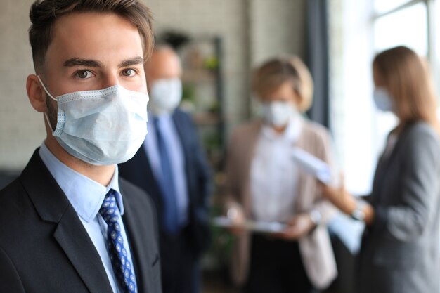 Zakenman met medisch masker met collega's op de achtergrond op kantoor.