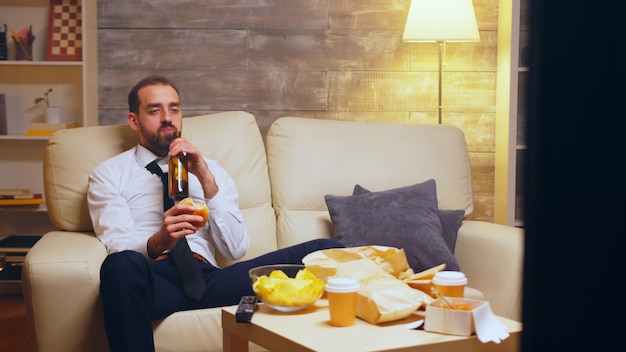 Zakenman met stropdas zittend op de bank een hamburger eten en praten aan de telefoon.