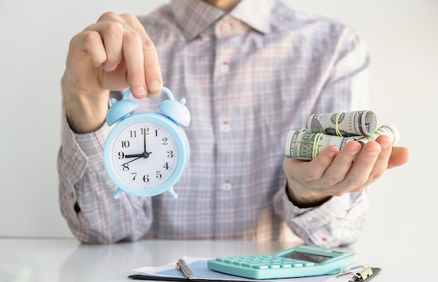Zakenman met wekker en stapel contant geld in de hand Tijd is geldconcept en belastingtijd