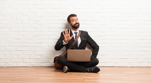 Zakenman met zijn laptop zittend op de vloer vijf met de vingers tellen