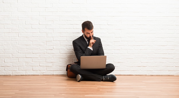 Zakenman met zijn laptop zitting op de vloer die een teken van sluitend mond en stiltegebaar toont