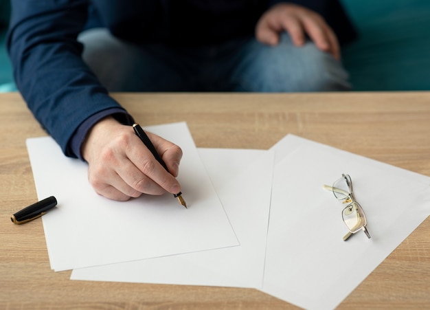 Zakenman op kantoor schrijft een brief of ondertekent een document op een stuk wit papier met een vulpen met punt. Close-up van handen van een zakenman in een pak
