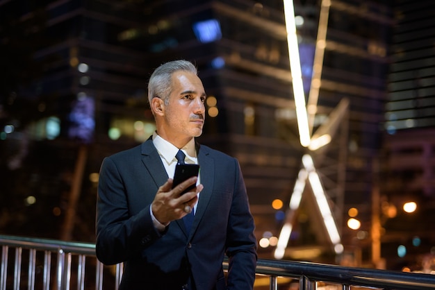 Zakenman pak dragen in de stad 's nachts tijdens het gebruik van de mobiele telefoon