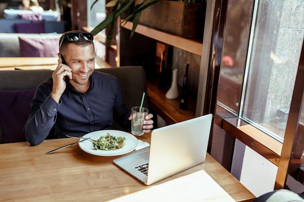 Zakenman praat aan de telefoon, luncht en werkt op laptop in restaurant. afstandswerk.