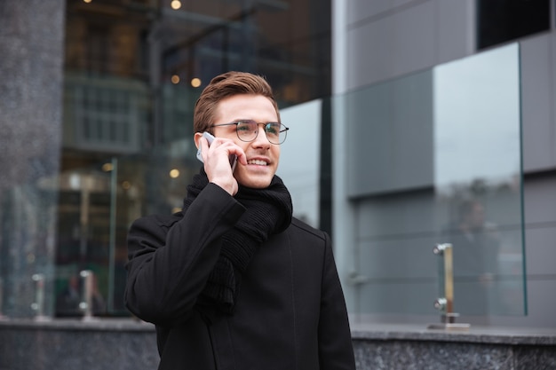 Zakenman praten aan de telefoon in de buurt van het kantoor. man met bril