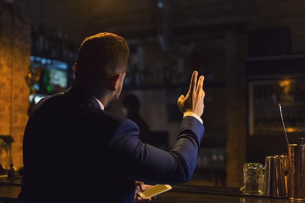 Zakenman rust op vrijdagavond, zit aan de toog en bestelt bier in de bar, gebaart naar barman, kopieer ruimte