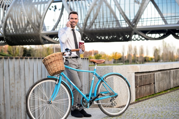 Zakenman staande bij zijn vintage fiets spreken op de mobiele telefoon