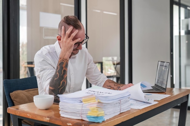 zakenman stress papierwerk en deadline concept benadrukte zakenman met papieren en grafieken zittend aan tafel in kantoor