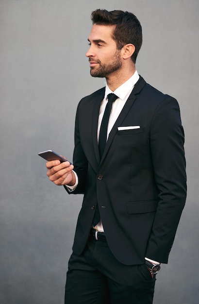 Zakenman telefoon en zelfvertrouwen met tech idee en sociale media break in studio pak corporate en executive mode met mobiele netwerken werknemer en professionele stijl met grijze achtergrond