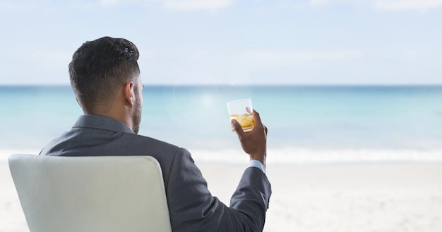 Zakenman terug zittend in stoel met glas drinken en zee