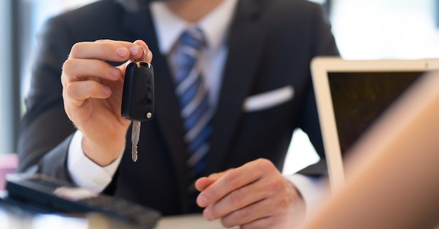 Zakenman van middelbare leeftijd met baard geeft de autosleutel aan de klantenservice bij het auto-onderhoudsstation en de autoservicegarage