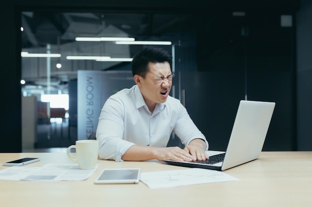 Zakenman wanhoop aziatische man aan het werk in kantoor kijken naar laptop scherm