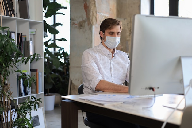 Zakenman werkt in preventief medisch masker op kantoor.