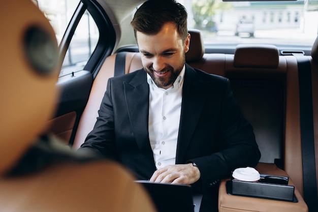 Zakenman zit op de achterbank van de auto en werkt aan een laptop.