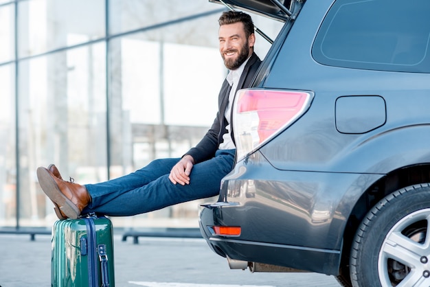 Zakenman zittend met koffer in de kofferbak tijdens de zakenreis. Zakelijk reizen per auto concept