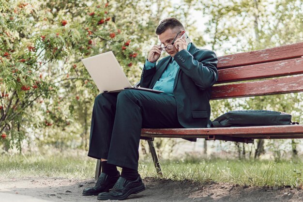 Zakenman zittend op de bank en kijken op de laptop in stadspark buiten. Knappe man aan het werk op zijn laptop. Dankzij de internetverbinding kunnen mensen overal werken.