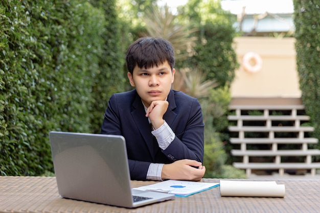 Zakenmanconcept een jonge zakenman in marinepak die in de tuin zit met de documenten en de laptop op tafel die er attent en serieus uitziet.