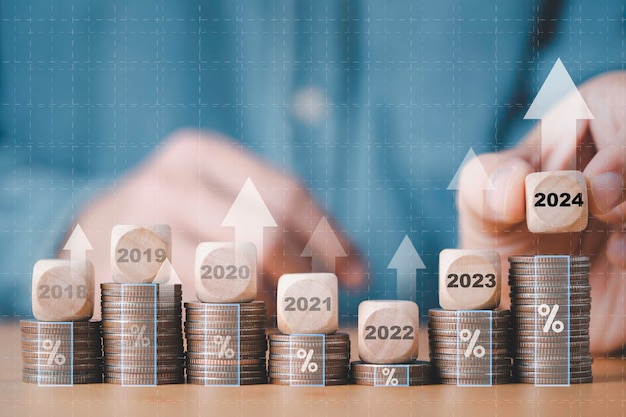 Zakenmanhand die houten blokkubus 2024 op muntstukken stapelen die voor opstellingsdoelstelling bedrijfskosten en begroting schaven van nieuw jaarconcept stapelen