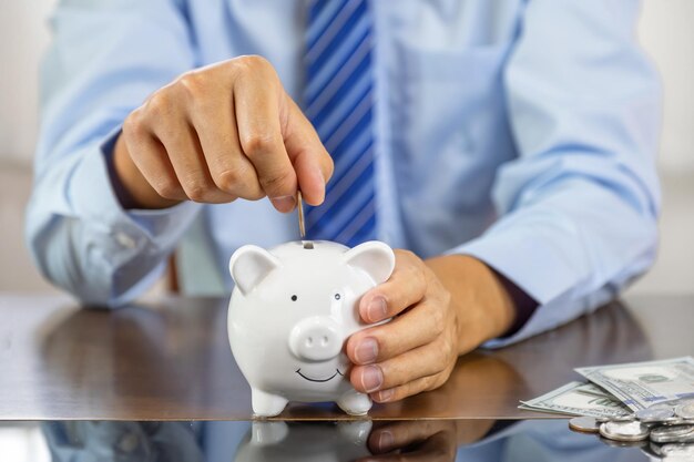 Foto zakenmanhand die muntstuk in blauw spaarvarken zetten dat geld bespaart voor toekomstig investeringsplan en pensioenfondsconcept