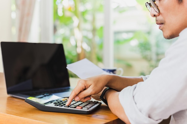 Zakenmanhand op rekenmachine om financieel rapport en laptopcomputer op tafel te berekenen